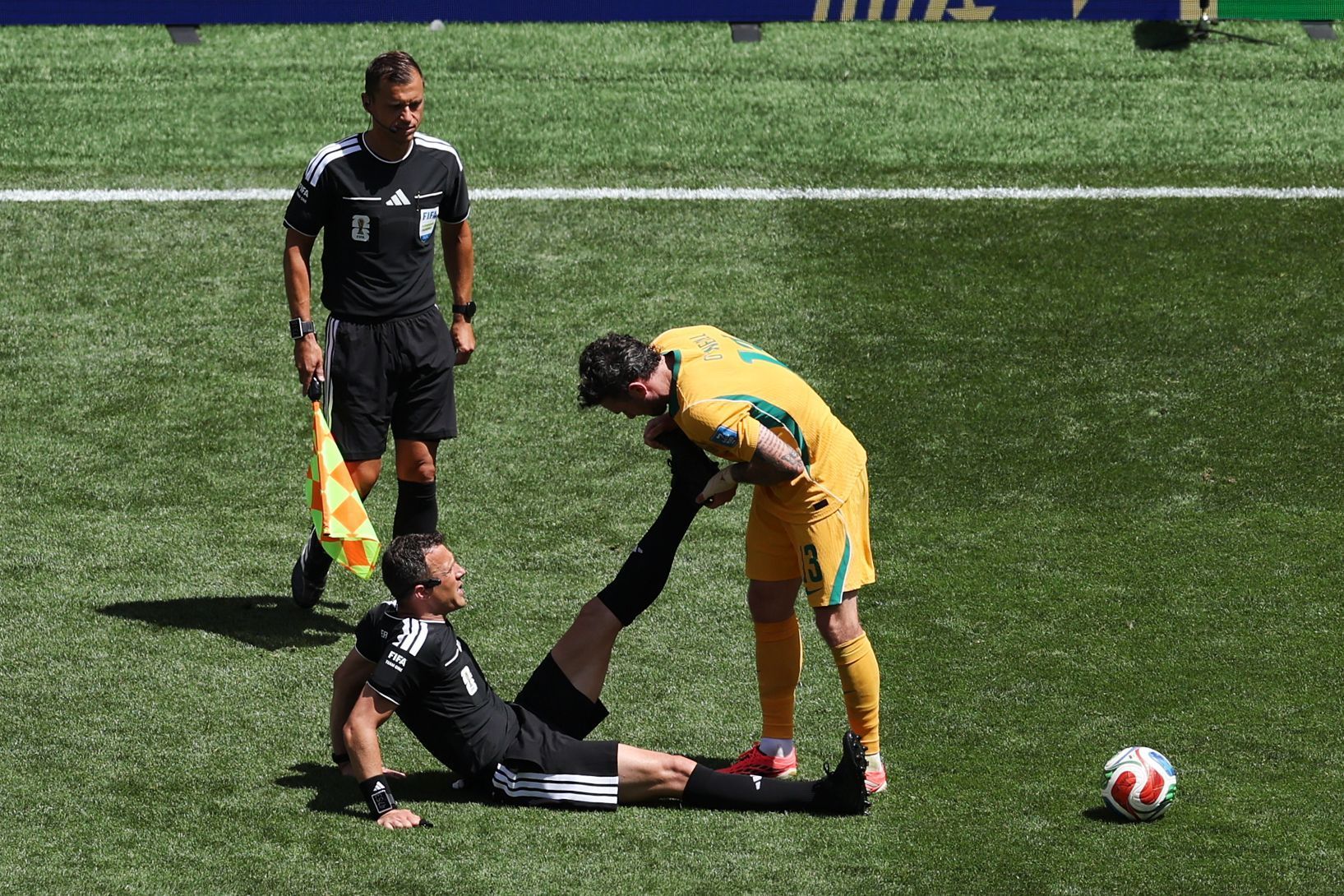 Schiedsrichter Felix Zwayer (Deutschland) sitzt auf dem Rasen und bekommt vom Australier Aiden O'Neill Unterstützung.