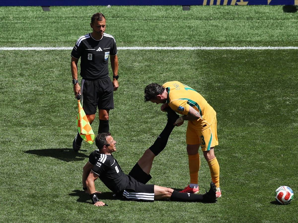 Schiedsrichter Felix Zwayer (Deutschland) sitzt auf dem Rasen und bekommt vom Australier Aiden O'Neill Unterstützung.