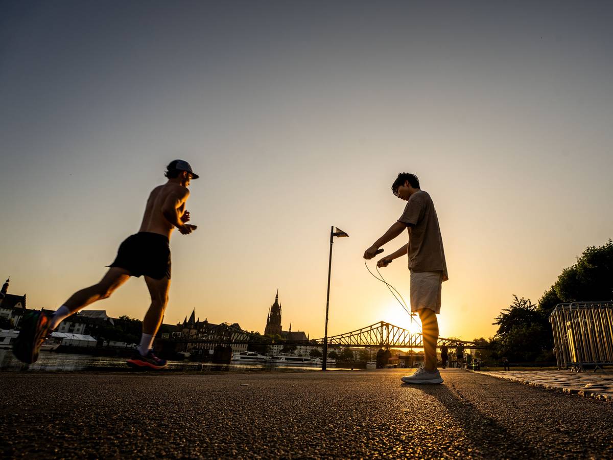 Menschen treiben bei Sonnenaufgang Frühsport am Mainufer.