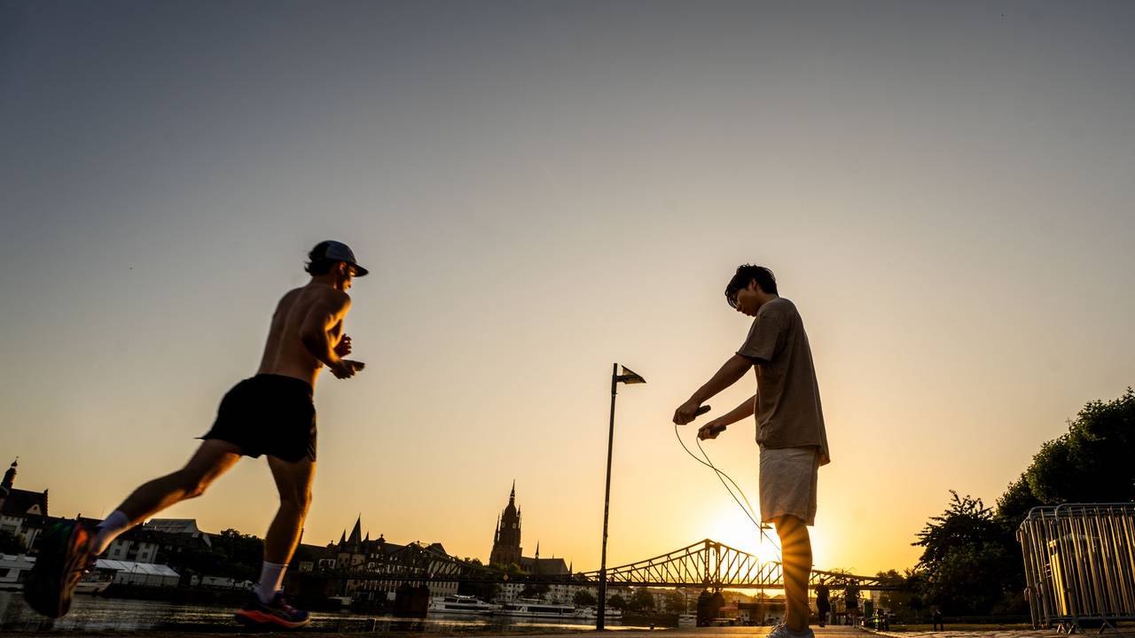 Menschen treiben bei Sonnenaufgang Frühsport am Mainufer.