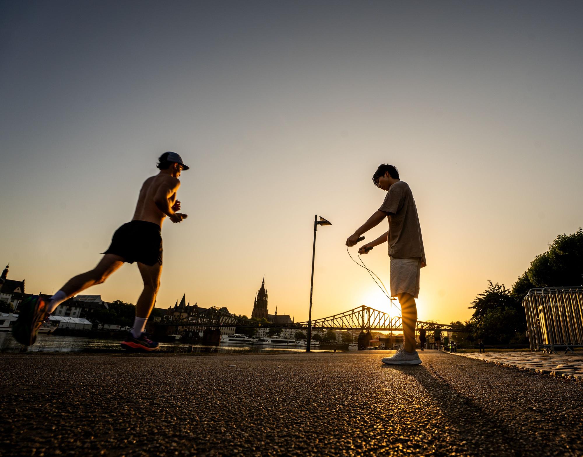 Menschen treiben bei Sonnenaufgang Frühsport am Mainufer.