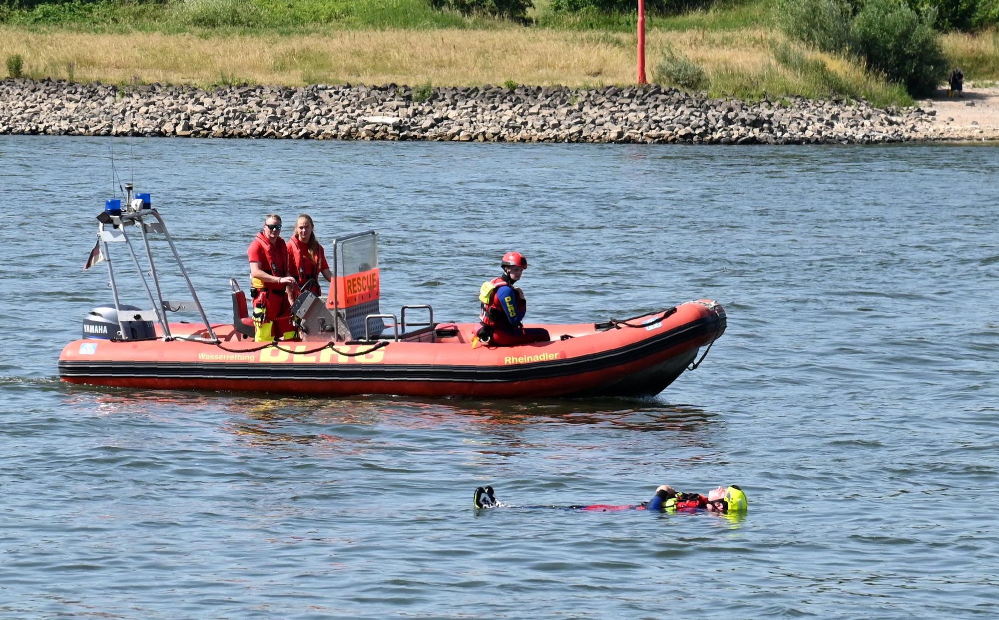 Ein Schwimmer der DLRG treibt neben einem Rettungsboot in Rückenlage auf dem Rhein.