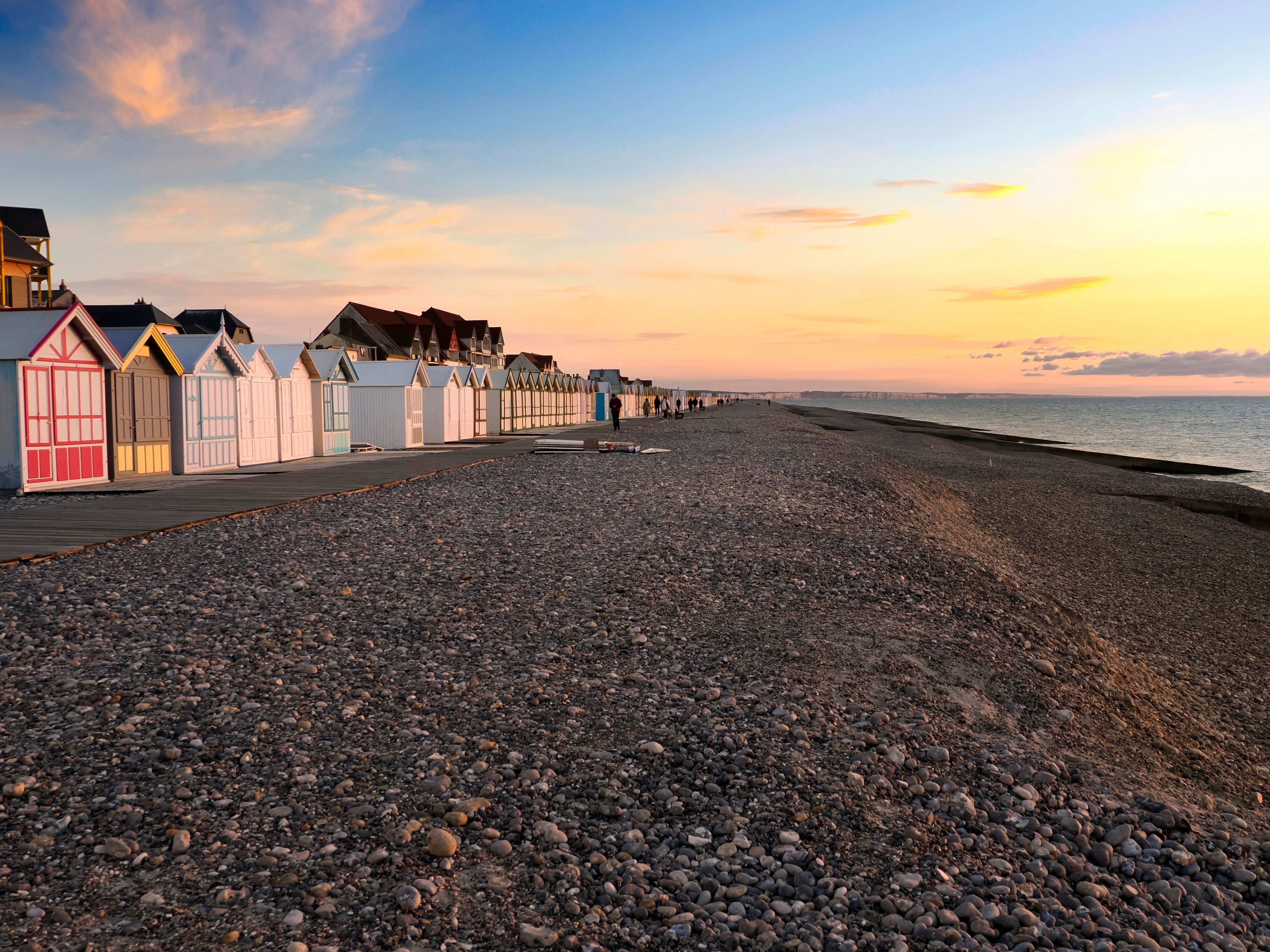 Ein Strand voller Steine und einer langen Reihe bunter Badehäuschen im Sonnenuntergang