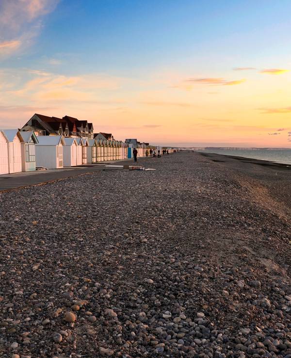 Ein Strand voller Steine und einer langen Reihe bunter Badehäuschen im Sonnenuntergang