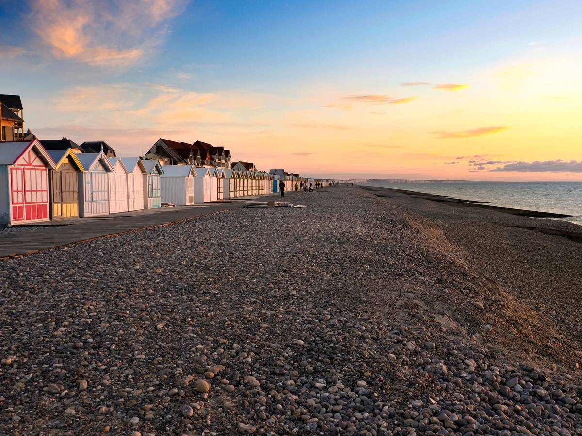 Ein Strand voller Steine und einer langen Reihe bunter Badehäuschen im Sonnenuntergang