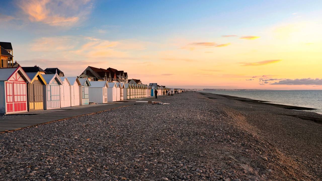 Ein Strand voller Steine und einer langen Reihe bunter Badehäuschen im Sonnenuntergang