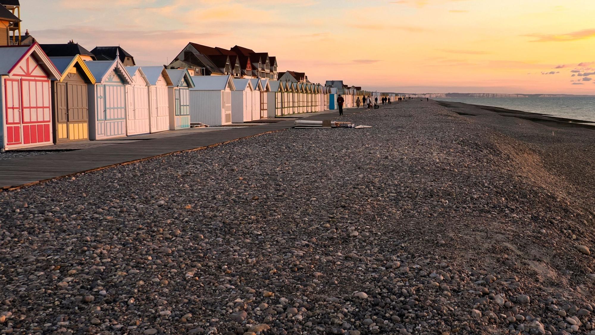 Ein Strand voller Steine und einer langen Reihe bunter Badehäuschen im Sonnenuntergang
