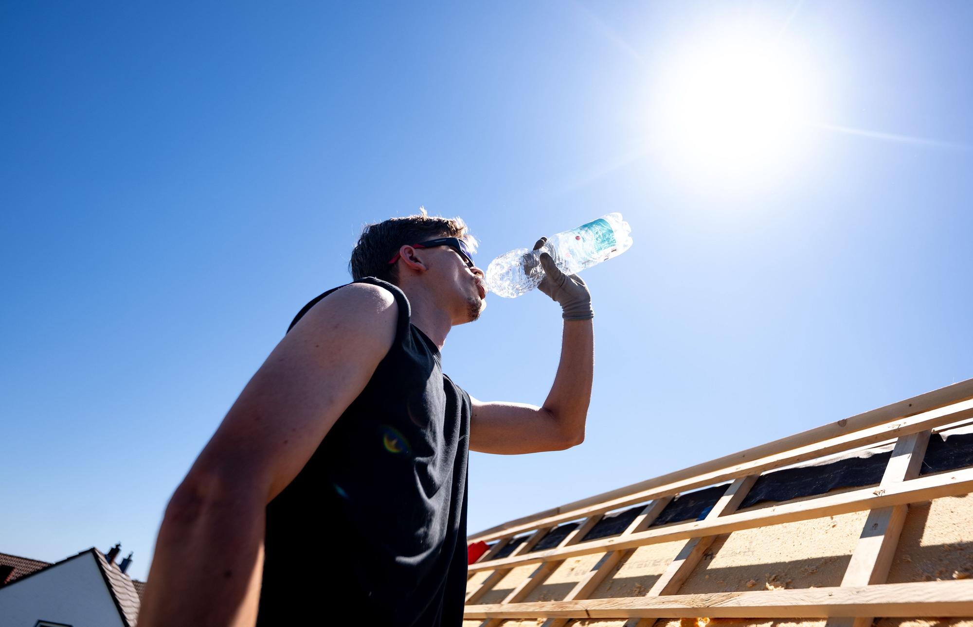 Ein Dachdecker trinkt Wasser unter der sengenden Sonne bei über 30 Grad auf dem Dach eines Hauses im Rhein-Sieg-Kreis.