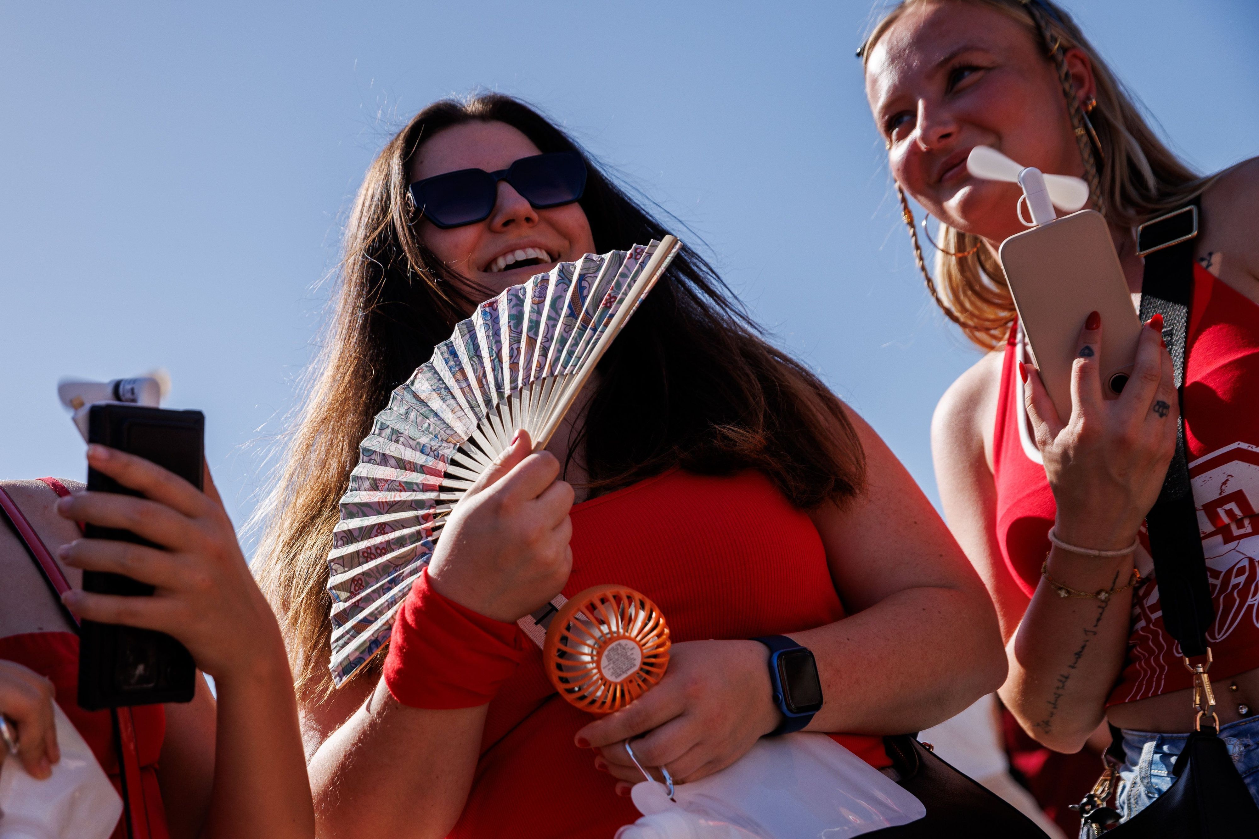 Zwei junge Frauen halten auf dem Weg zum Konzert des US-amerikanischen Musikers Bruno Mars im Olympiastadion zur Kühlung einen Fächer und einen Taschenventilator in der Hand.