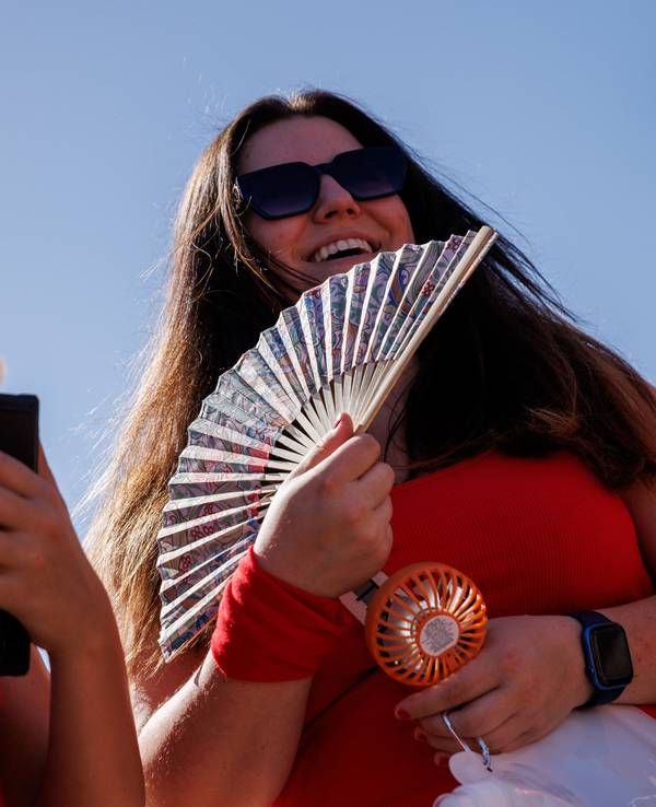 Zwei junge Frauen halten auf dem Weg zum Konzert des US-amerikanischen Musikers Bruno Mars im Olympiastadion zur Kühlung einen Fächer und einen Taschenventilator in der Hand.