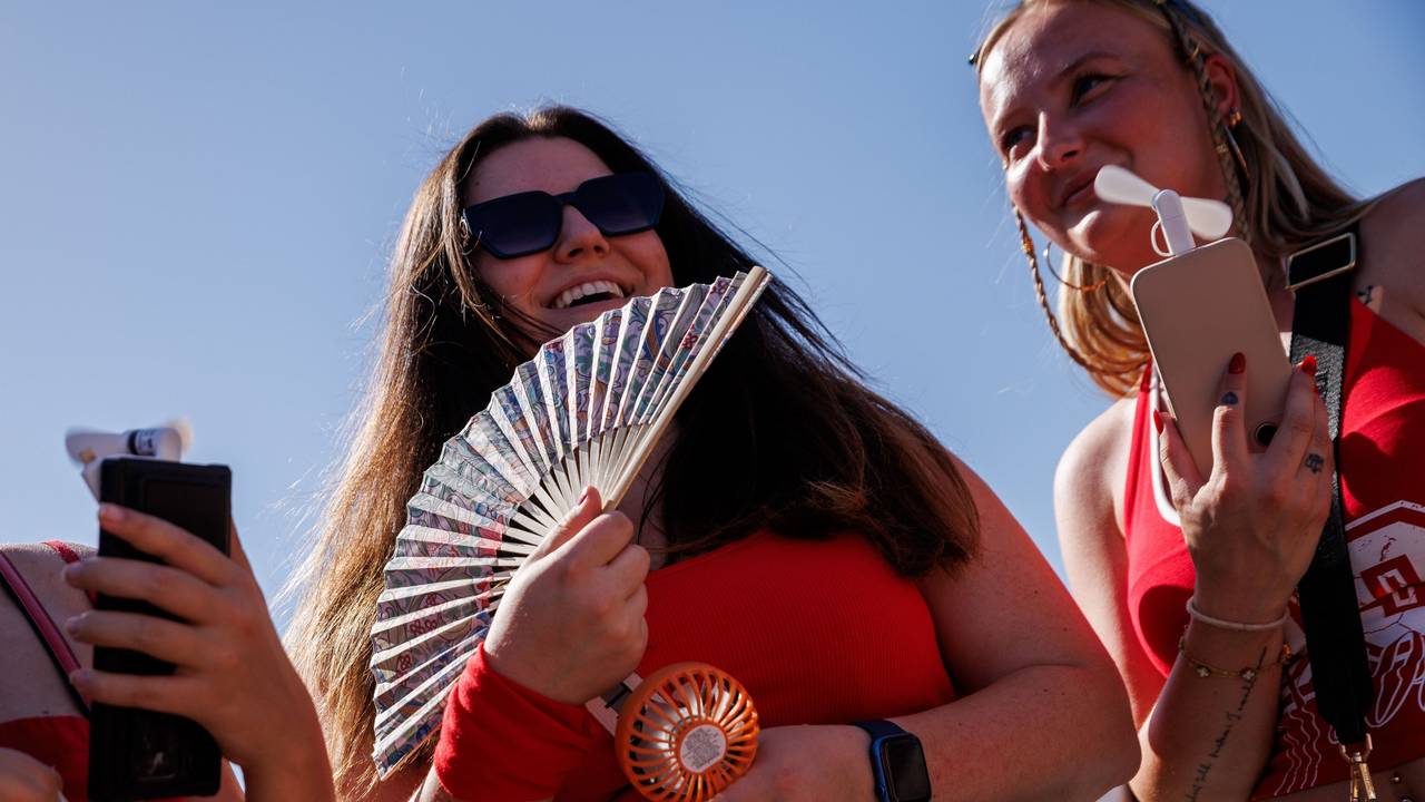 Zwei junge Frauen halten auf dem Weg zum Konzert des US-amerikanischen Musikers Bruno Mars im Olympiastadion zur Kühlung einen Fächer und einen Taschenventilator in der Hand.