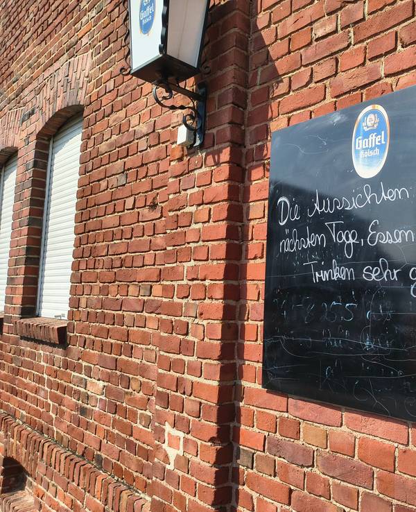 Auf einer Tafel an der Gaststätte in Köln-Merkenich in Langel werden Besucher noch herzlich empfangen. Bald schließt die Gastro in Rheinnähe.