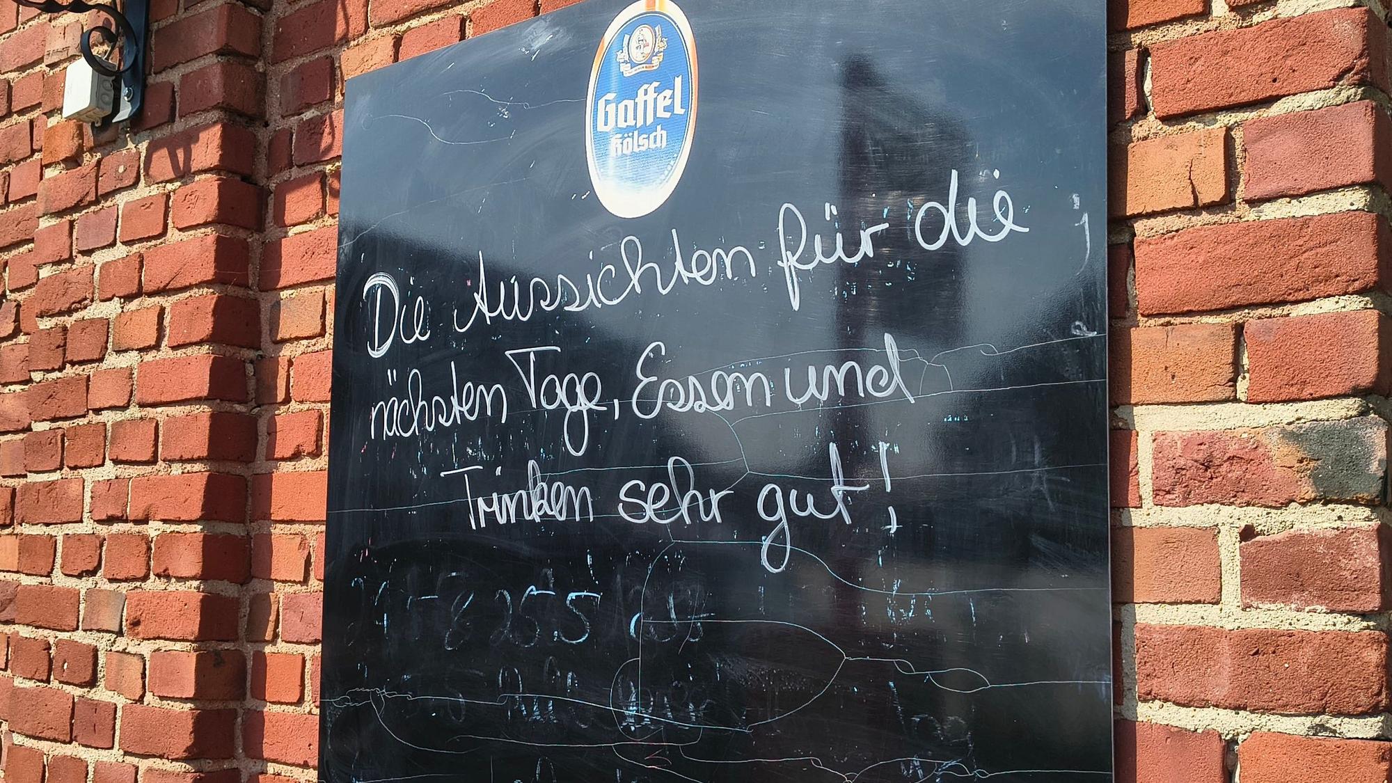 Auf einer Tafel an der Gaststätte in Köln-Merkenich in Langel werden Besucher noch herzlich empfangen. Bald schließt die Gastro in Rheinnähe.