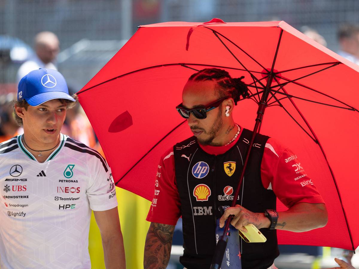 Lewis Hamilton schützt sich unter einem roten Schirm vo der Sonne, neben ihm geht Kimi Antonelli.