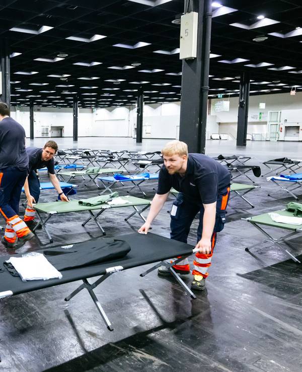 Helfer bauen das Notfallversorgungszentrum in einer Messehalle auf.