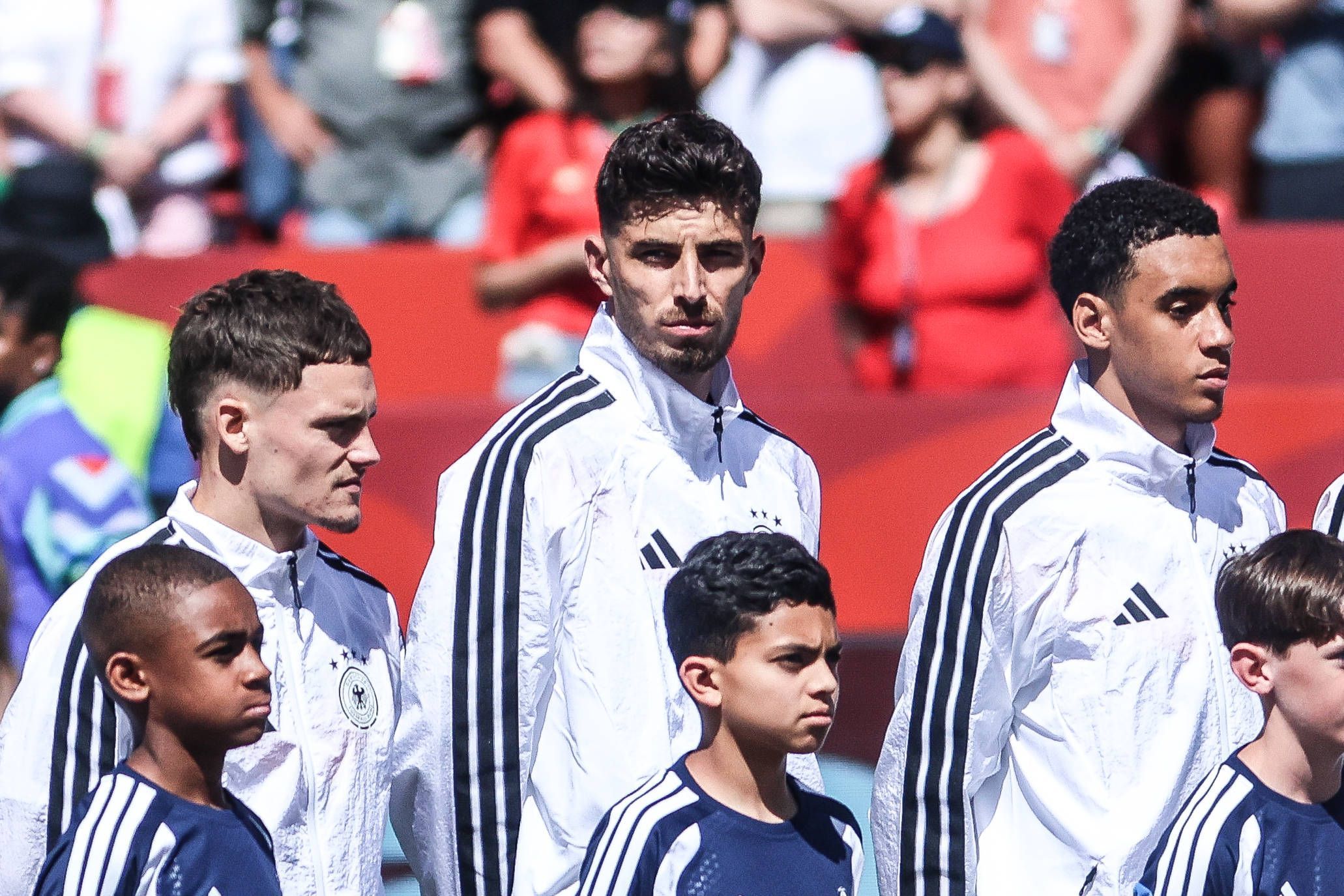 Florian Wirtz, Kai Havertz und Jamal Musiala stehen vor einem Spiel während der Hymne nebeneinander.