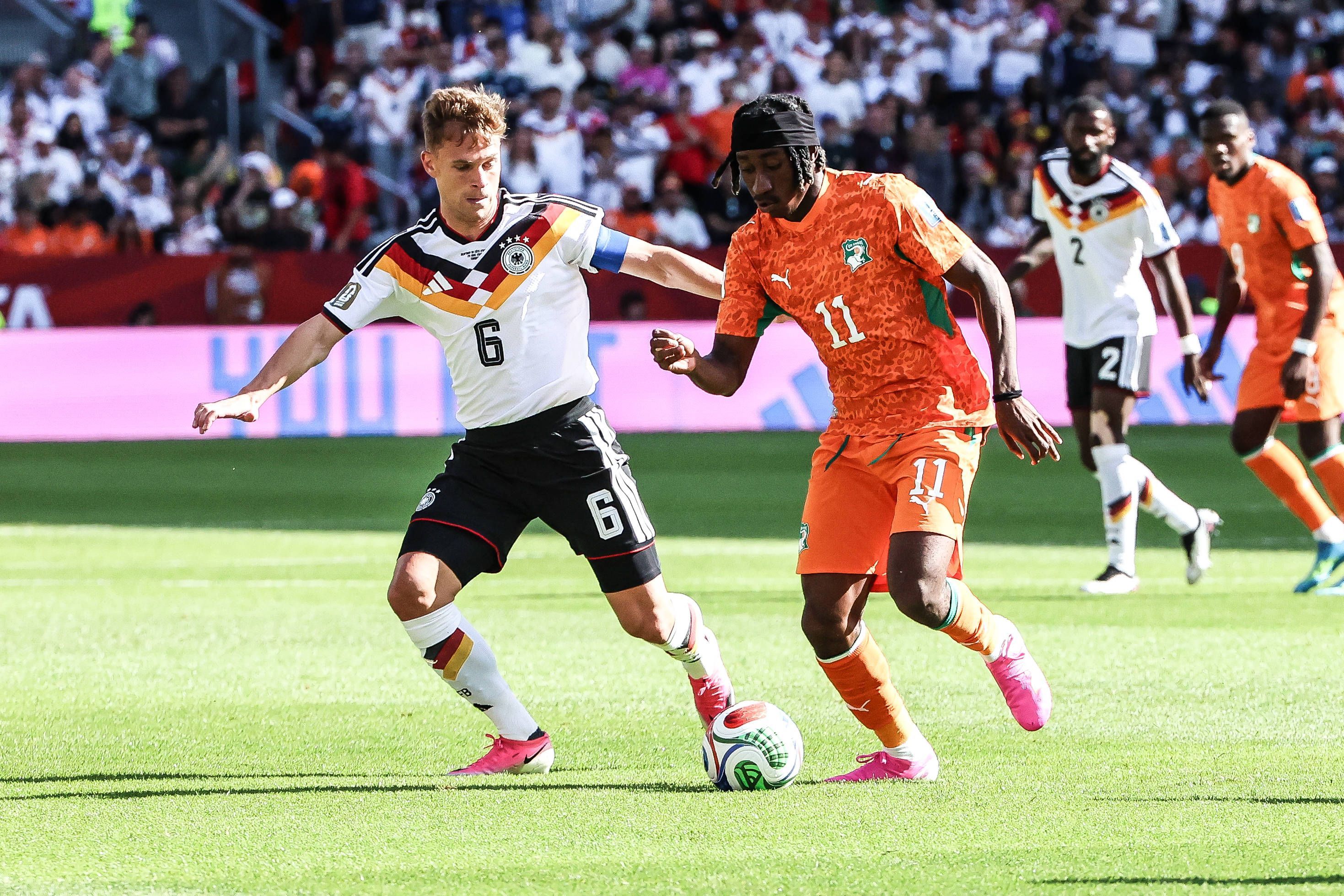 Joshua Kimmich mit weißem Trikot und schwarzer Hose im Zweikampf mit Yan Diomande.
