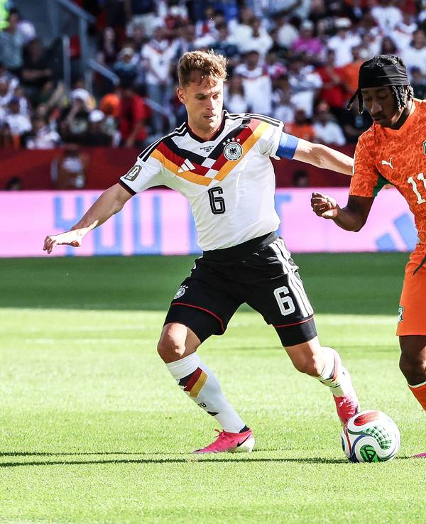 Joshua Kimmich mit weißem Trikot und schwarzer Hose im Zweikampf mit Yan Diomande.