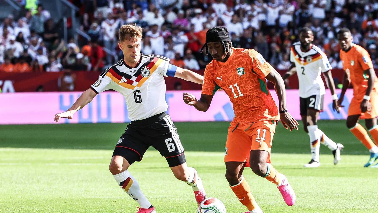 Joshua Kimmich mit weißem Trikot und schwarzer Hose im Zweikampf mit Yan Diomande.