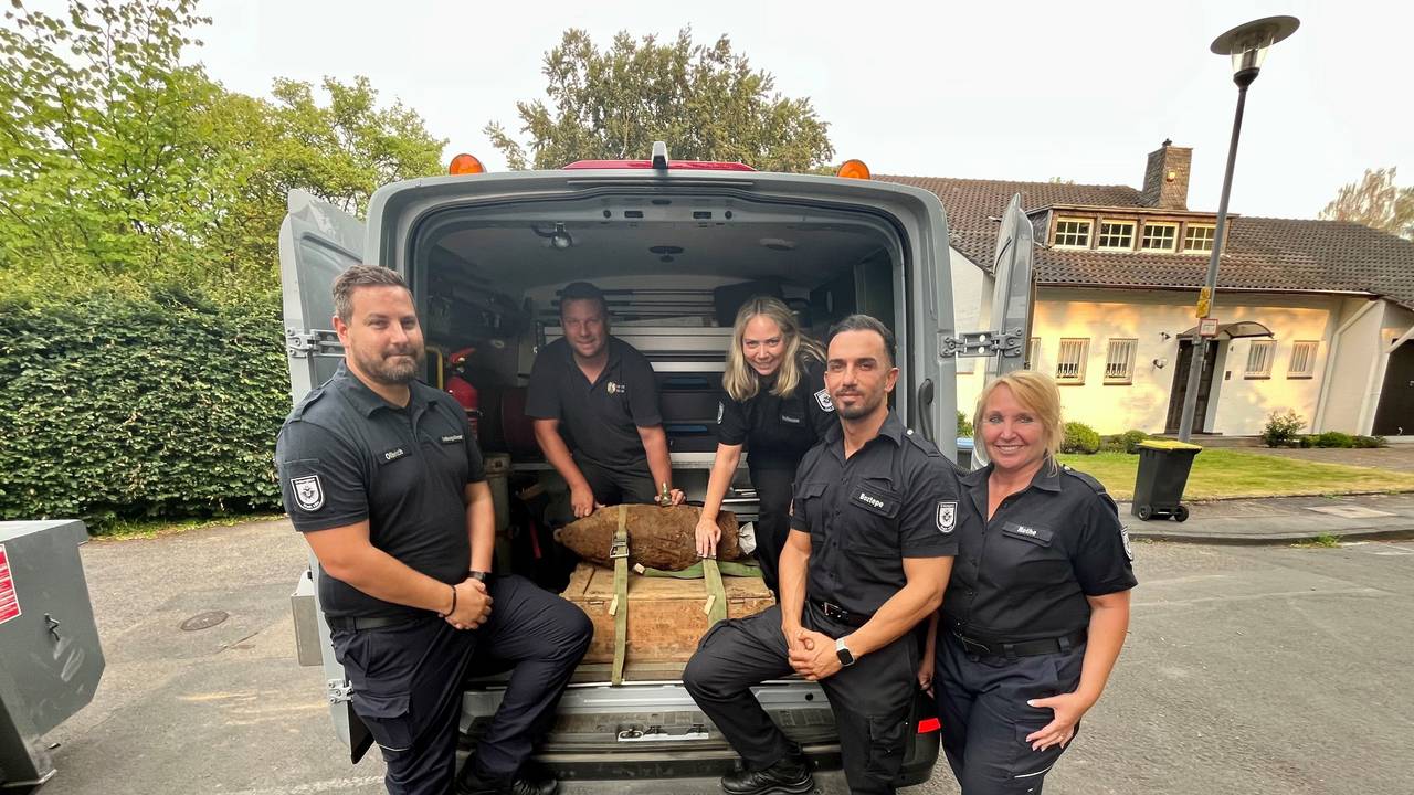 Karsten Olbrich, Silvana Hoffmann, Caner Boztepe und Petra Rothe (Leitungsteam Ordnungsamt) und hinten Philipp Blens (KBD Rheinland der Bezirksregierung Düsseldorf) zeigen den entschärften Blindgänger, der in einem Kleintransporter liegt.
