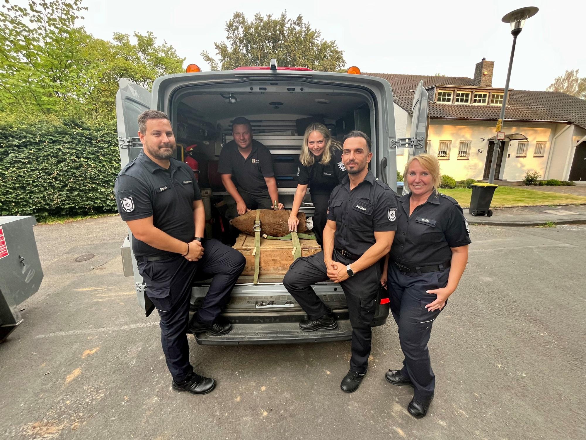 Karsten Olbrich, Silvana Hoffmann, Caner Boztepe und Petra Rothe (Leitungsteam Ordnungsamt) und hinten Philipp Blens (KBD Rheinland der Bezirksregierung Düsseldorf) zeigen den entschärften Blindgänger, der in einem Kleintransporter liegt.