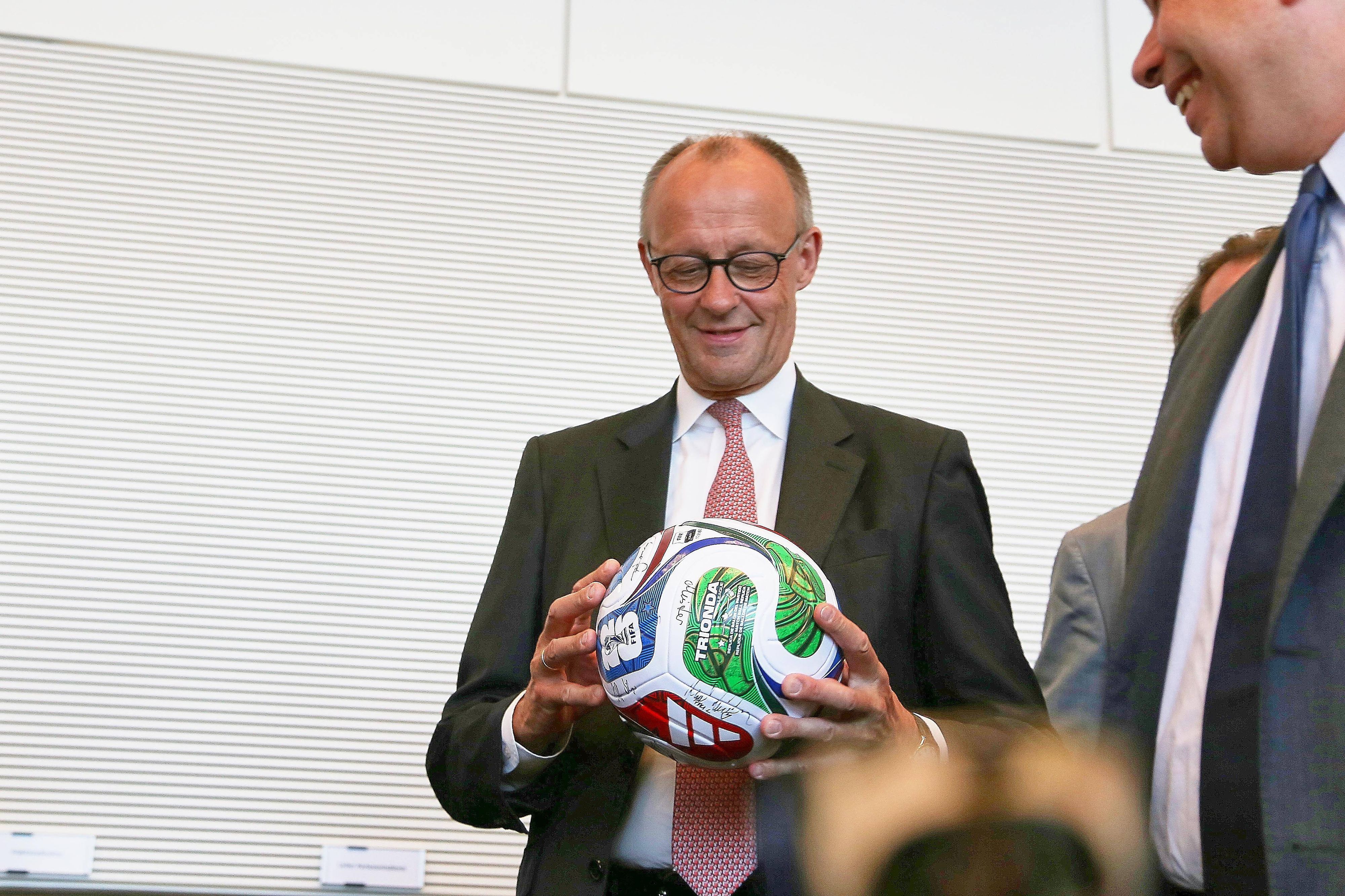 Bundeskanzler Friedrich Merz hält einen Fußball in der Hand.