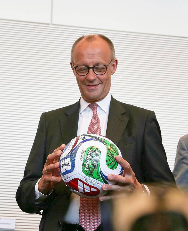Bundeskanzler Friedrich Merz hält einen Fußball in der Hand.