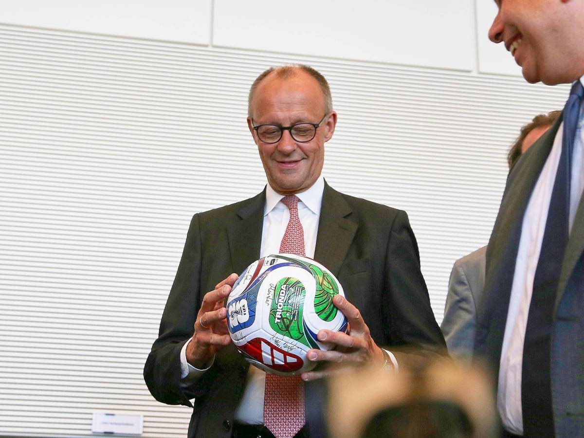 Bundeskanzler Friedrich Merz hält einen Fußball in der Hand.