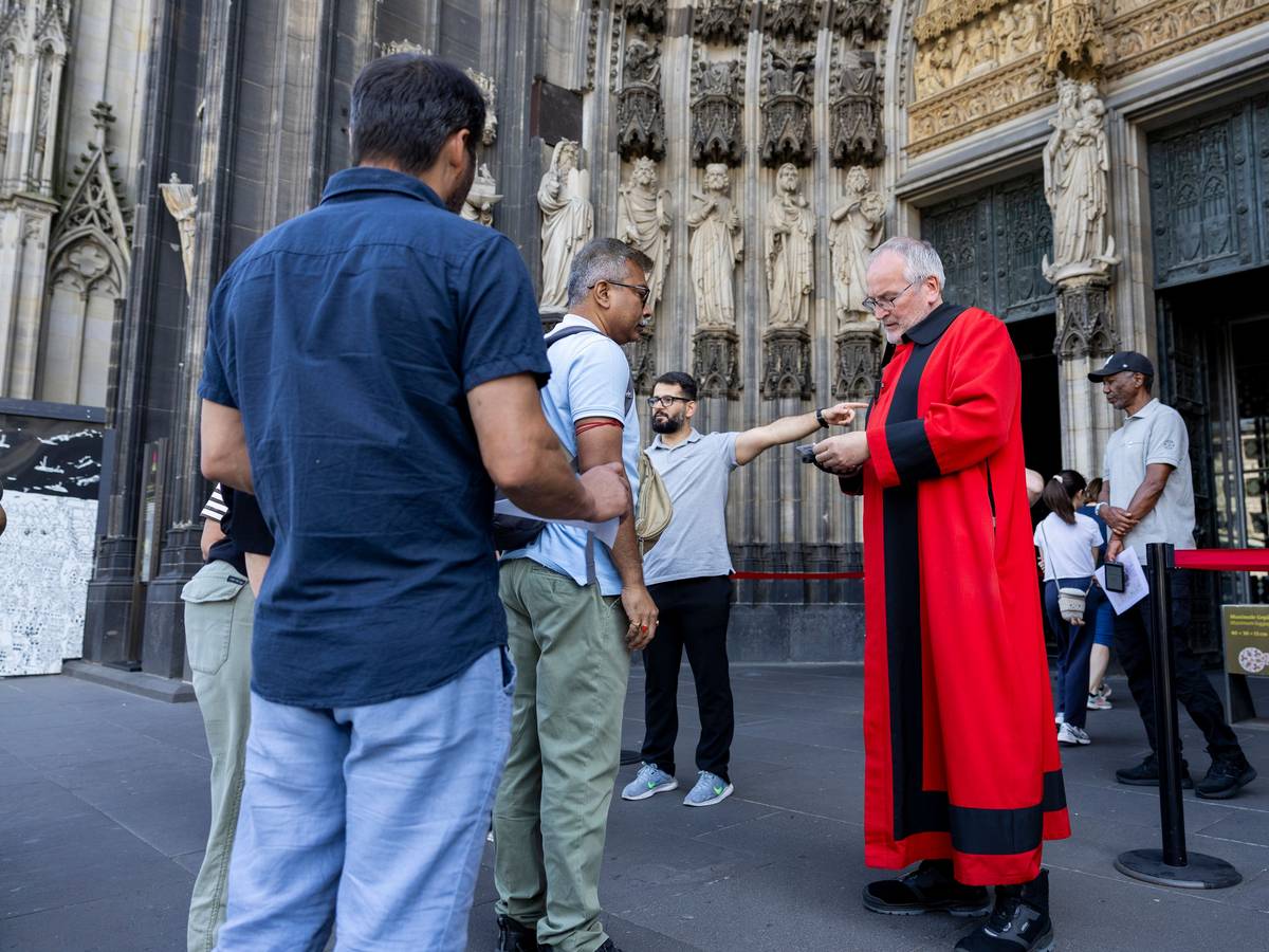 Domschweizer und Servicekräfte informieren Menschen vor dem Kölner Dom über die neuen Besuchsregeln.