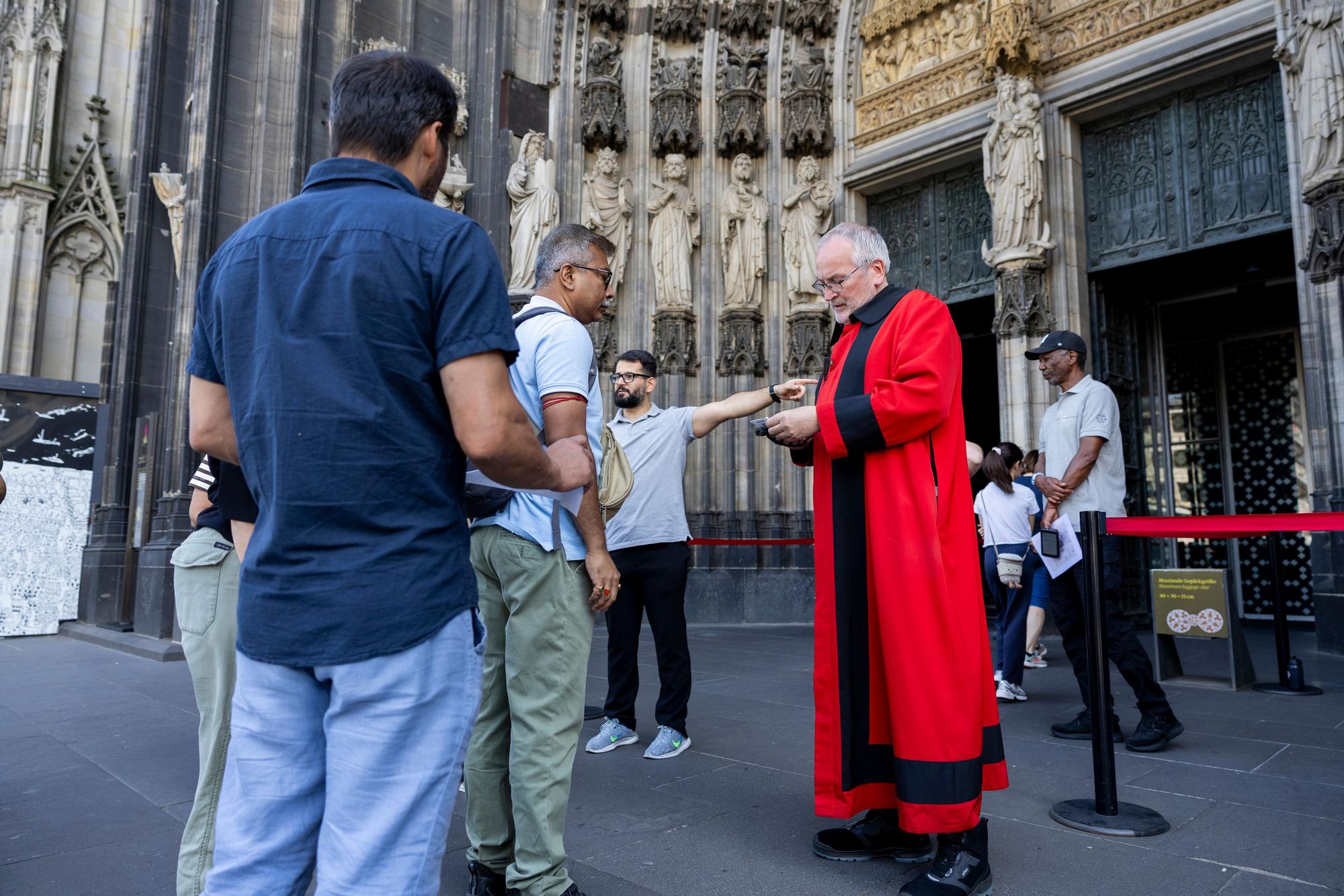 Domschweizer und Servicekräfte informieren Menschen vor dem Kölner Dom über die neuen Besuchsregeln.