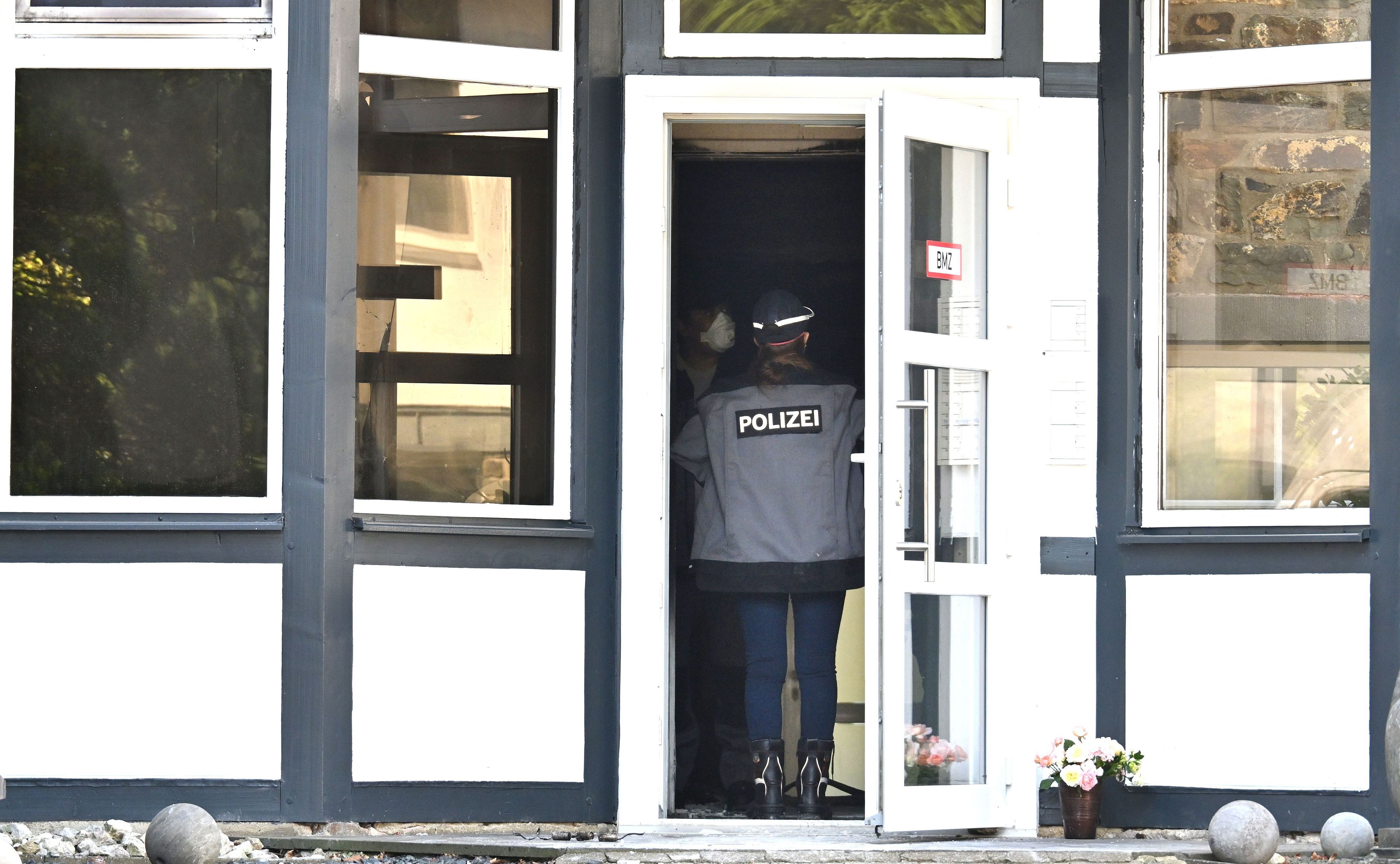 Eine Einsatzkraft der Polizei steht in einem Eingang zu einem Gebäude und spricht mit einer Person, die eine Maske trägt. Bei einem Brand hat es mehrere Tote gegeben.