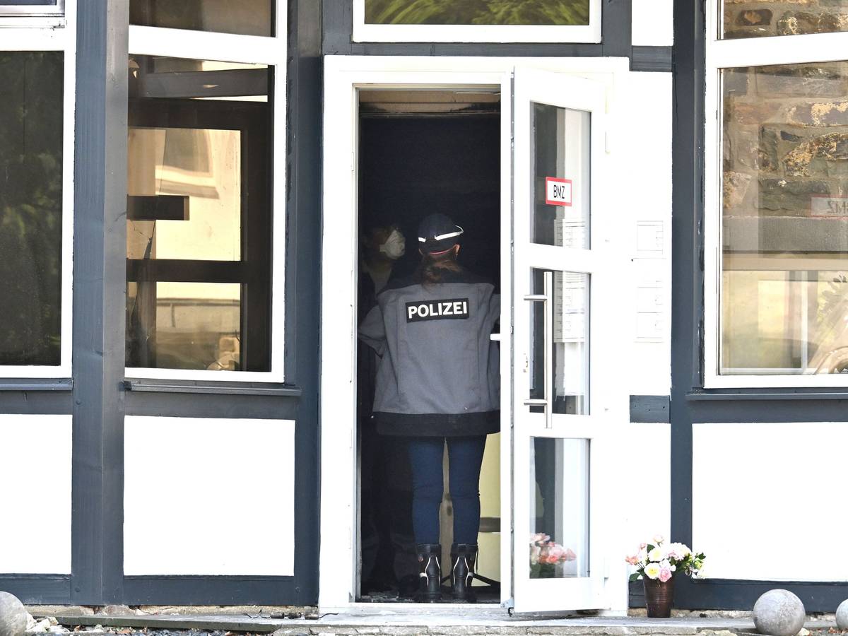 Eine Einsatzkraft der Polizei steht in einem Eingang zu einem Gebäude und spricht mit einer Person, die eine Maske trägt. Bei einem Brand hat es mehrere Tote gegeben.