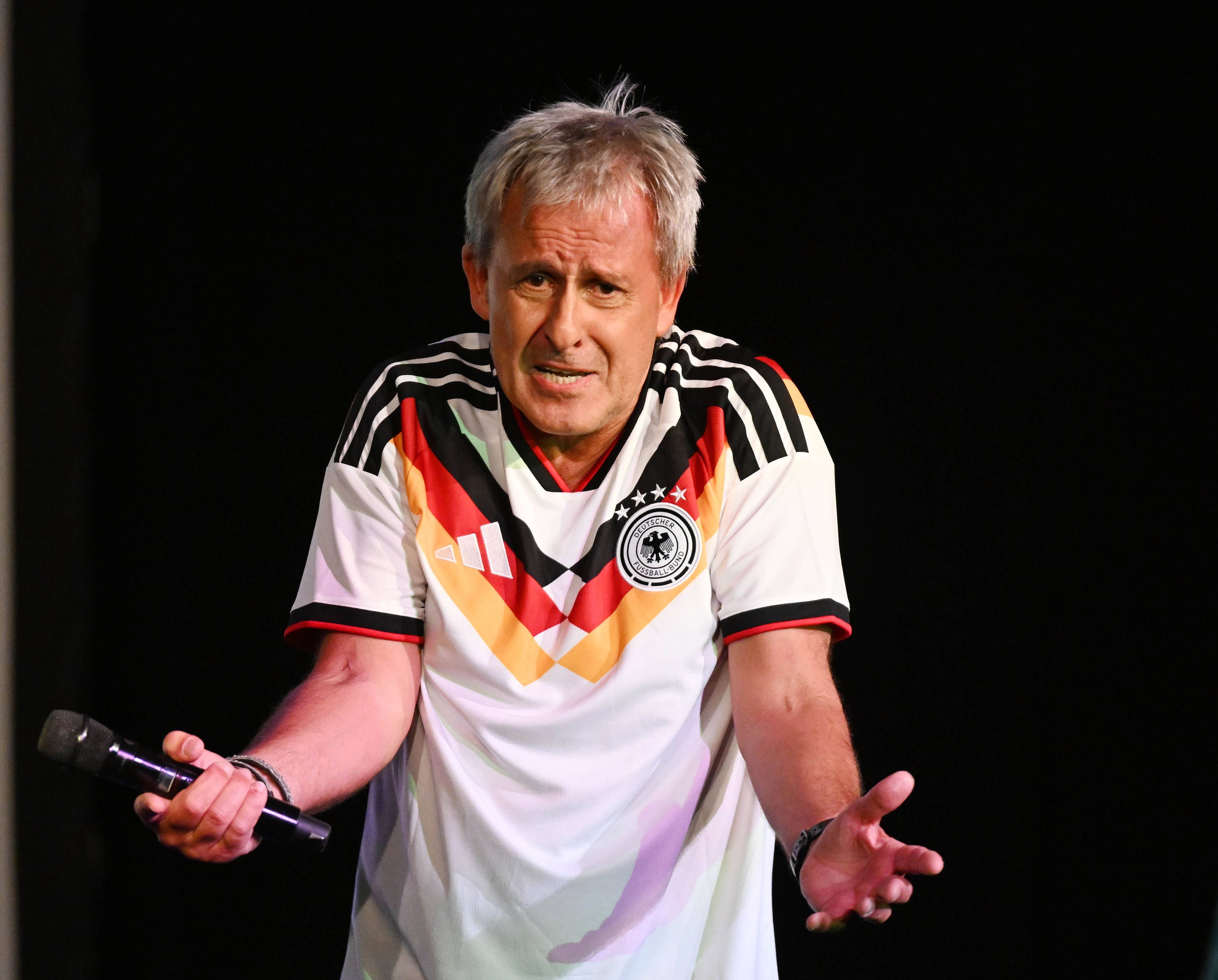 Pierre Littbarski mit Deutschland-Trikot und Mikrofon in der Hand auf der Bühne.