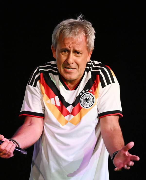 Pierre Littbarski mit Deutschland-Trikot und Mikrofon in der Hand auf der Bühne.