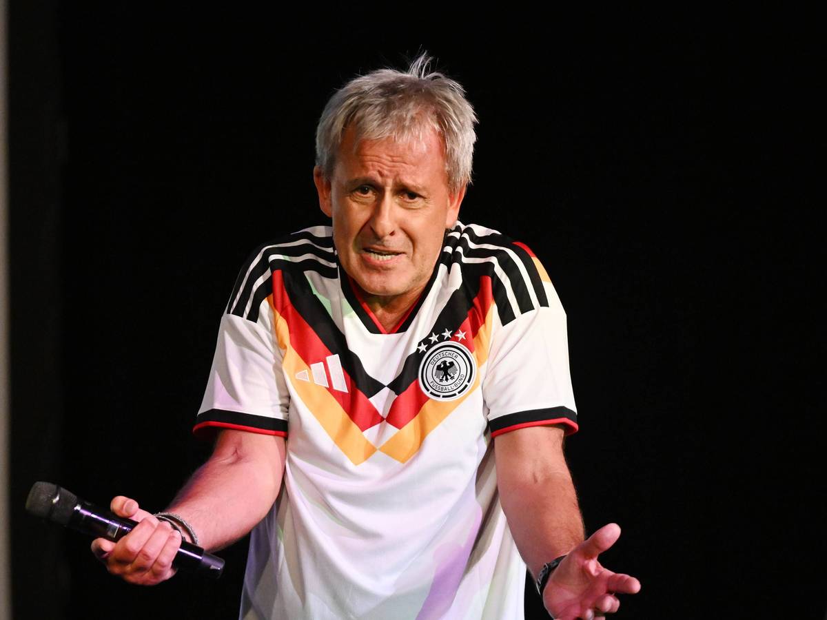 Pierre Littbarski mit Deutschland-Trikot und Mikrofon in der Hand auf der Bühne.