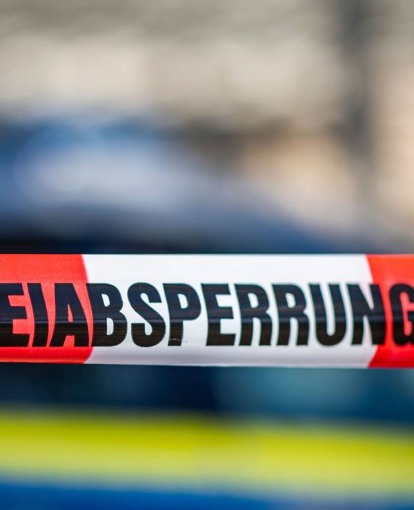 Ein Absperrband mit der Aufschrift „Polizeiabsperrung“ ist vor einem Polizeiwagen aufgespannt. (Symbolfoto)