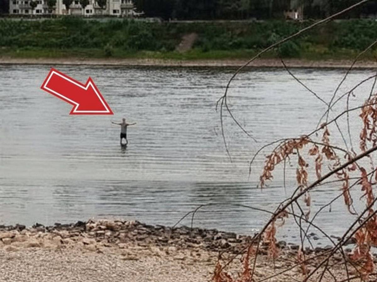 Ein Mann steht bei Niedrigwasser im Rhein in Köln-Niehl. Könnte man durch den Fluss laufen?