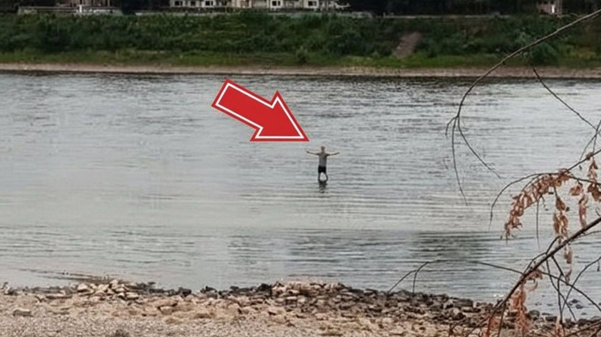 Ein Mann steht bei Niedrigwasser im Rhein in Köln-Niehl. Könnte man durch den Fluss laufen?