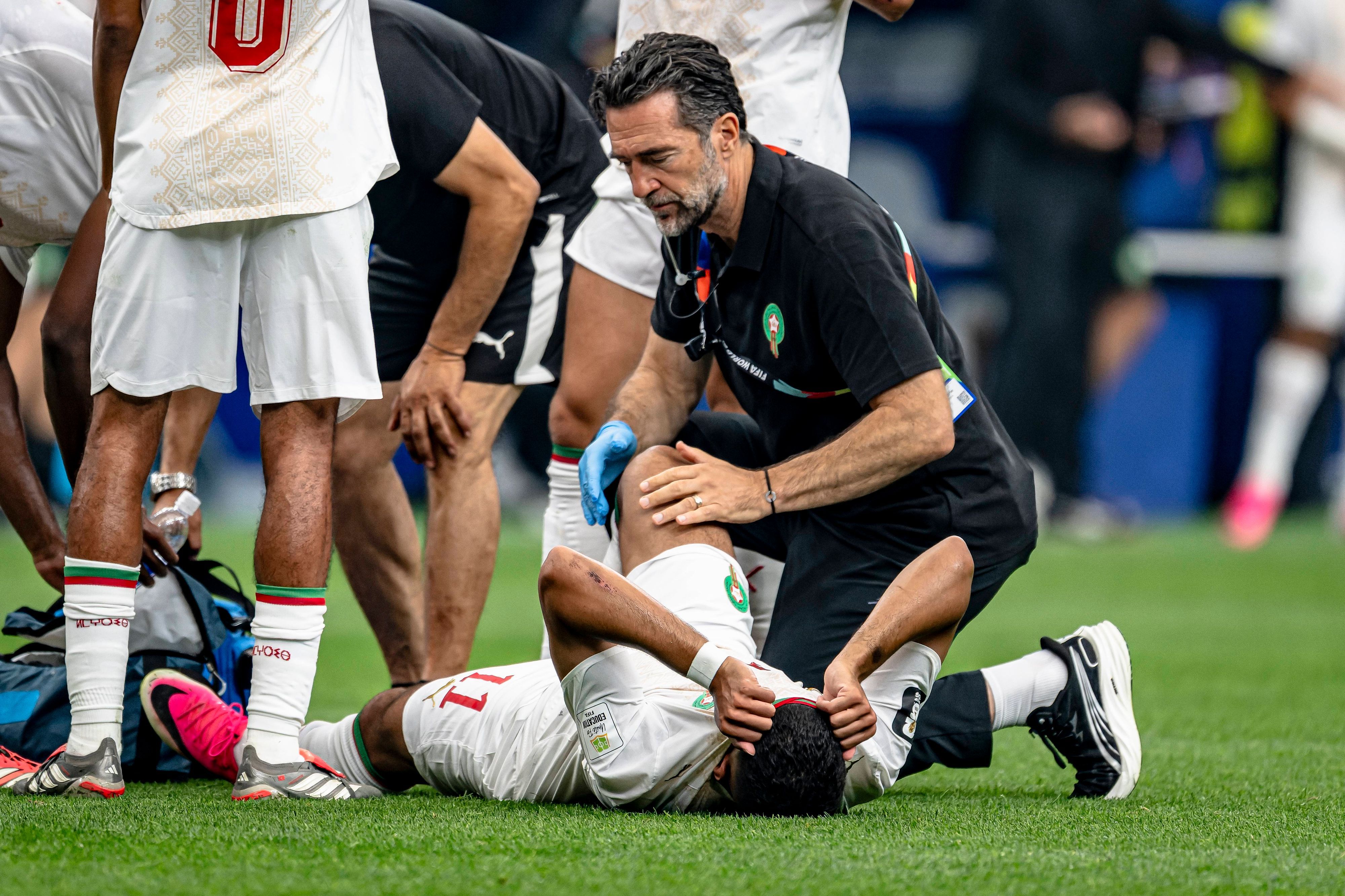 Marokkos Ismael Saibari liegt verletzt auf dem Rasen und wird von einem Physio behandelt. Dabei hat er sein Gesicht unter dem Trikot versteckt.