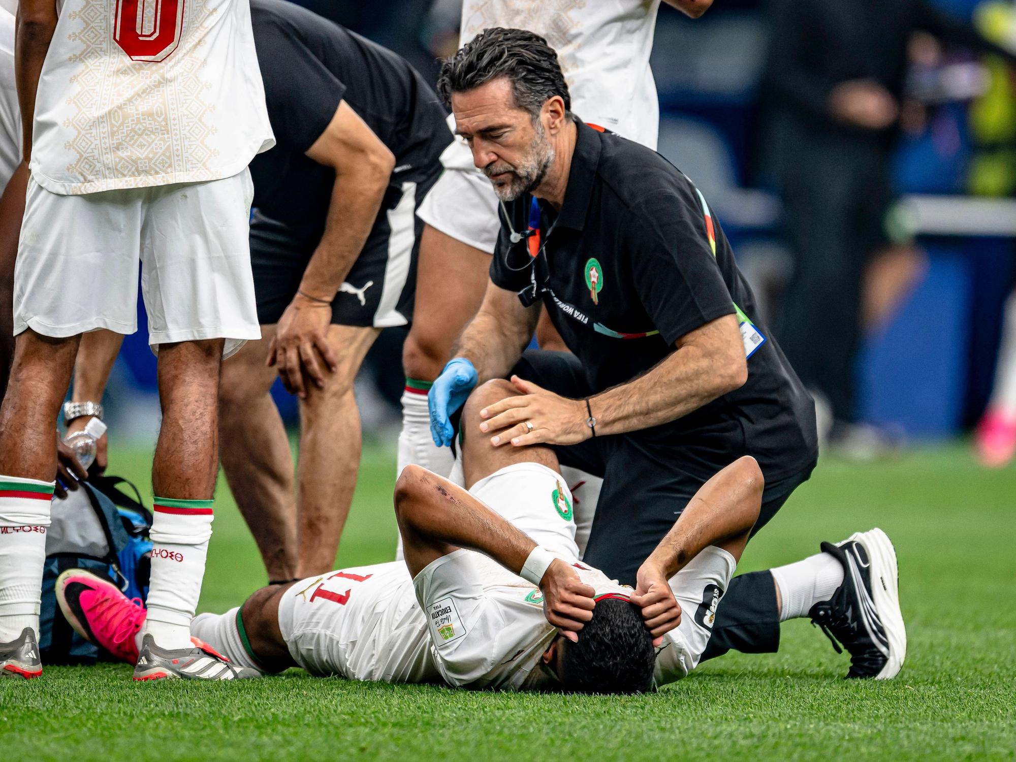 Marokkos Ismael Saibari liegt verletzt auf dem Rasen und wird von einem Physio behandelt. Dabei hat er sein Gesicht unter dem Trikot versteckt.