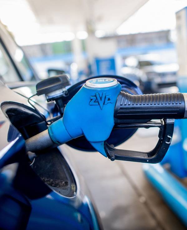 Eine Zapfpistole mit der Aufschrift „Super 95“ steckt an einer Tankstelle in der Tanköffnung eines Fahrzeugs.