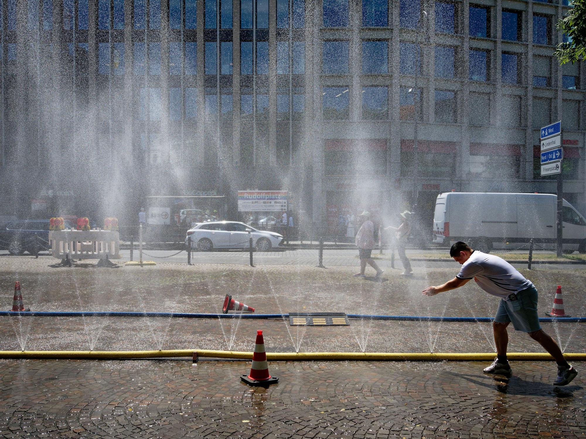 Passanten genießen Ende Juni Wasserfontänen, die im Rahmen der Hitzeaktion „Cooling Cologne“ der Stadt Köln auf dem Rudolfplatz in der Innenstadt installiert wurden.