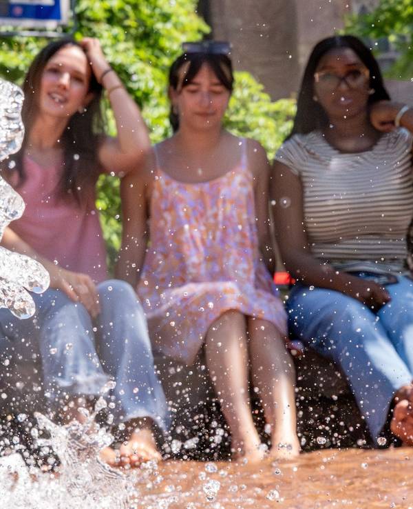 Drei junge Frauen kühlen sich bei sommerlichen Temperaturen über 30 Grad am Kaiserbrunnen in Bonn ab.