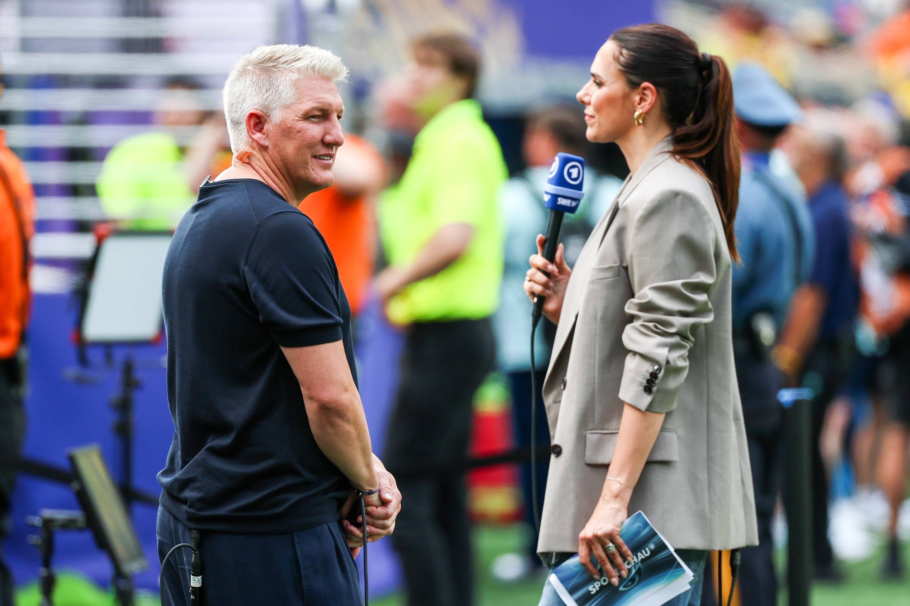 Bastian Schweinsteiger blickt sich neben Esther Sedlaczek bei der WM 2026 um.