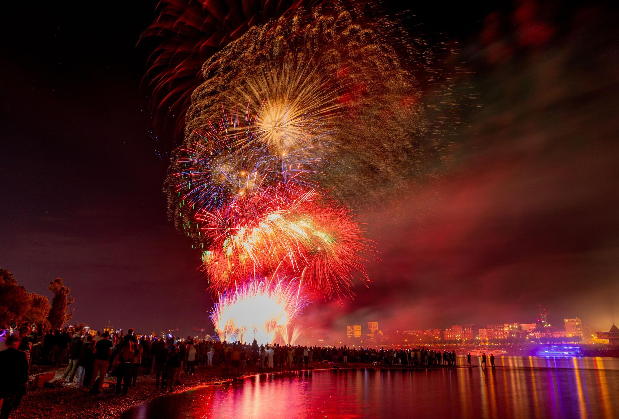 Menschen besuchen im Kölner Rheinpark das größte musiksynchrone Feuerwerk Europas.