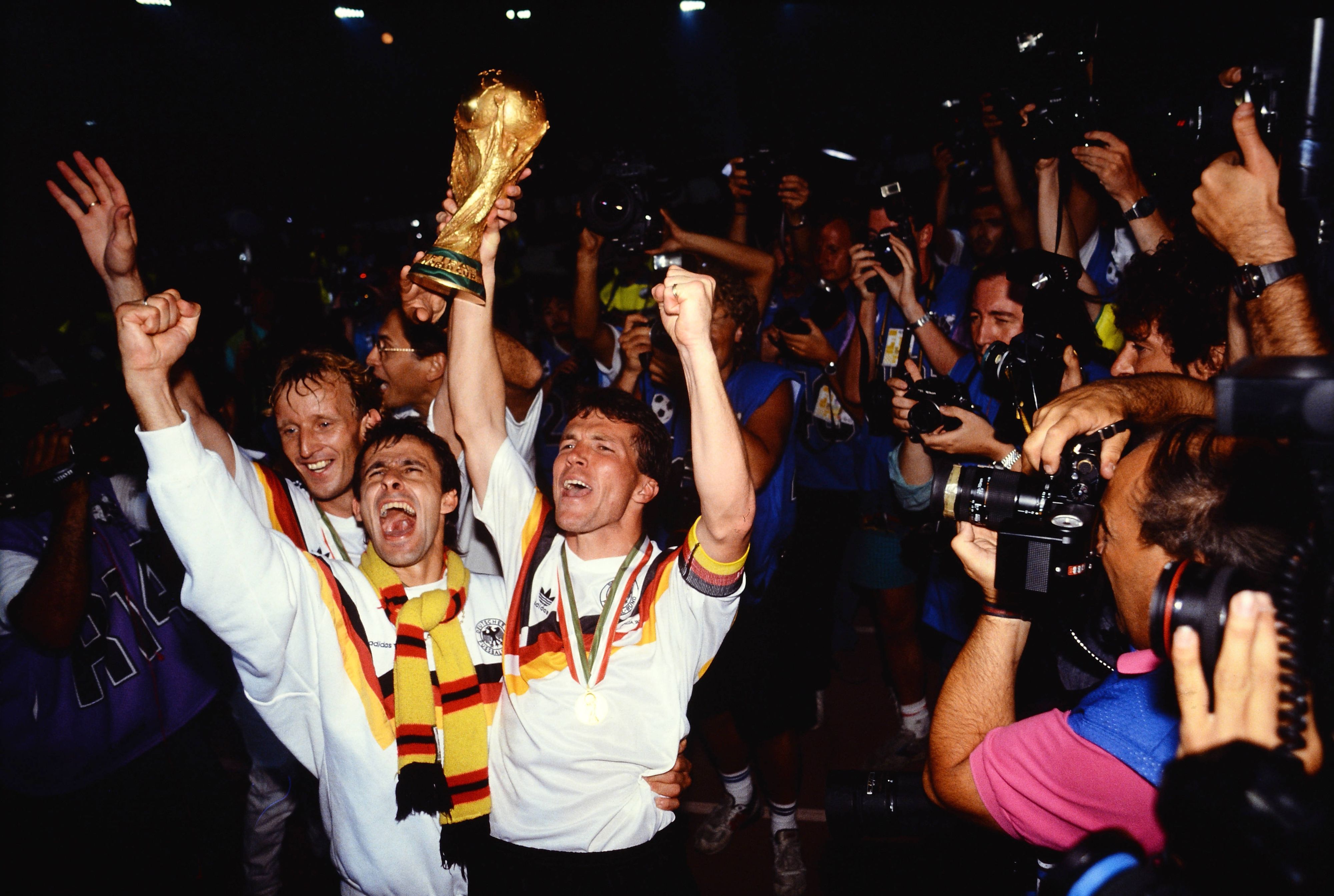Pierre Littbarski bejubelt mit Andreas Brehme und Lothar Matthäus umringt von Journalisten den deutschen WM-Sieg 1990.