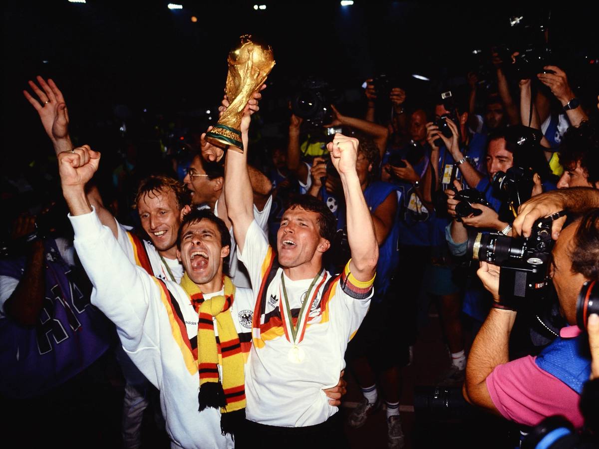Pierre Littbarski bejubelt mit Andreas Brehme und Lothar Matthäus umringt von Journalisten den deutschen WM-Sieg 1990.