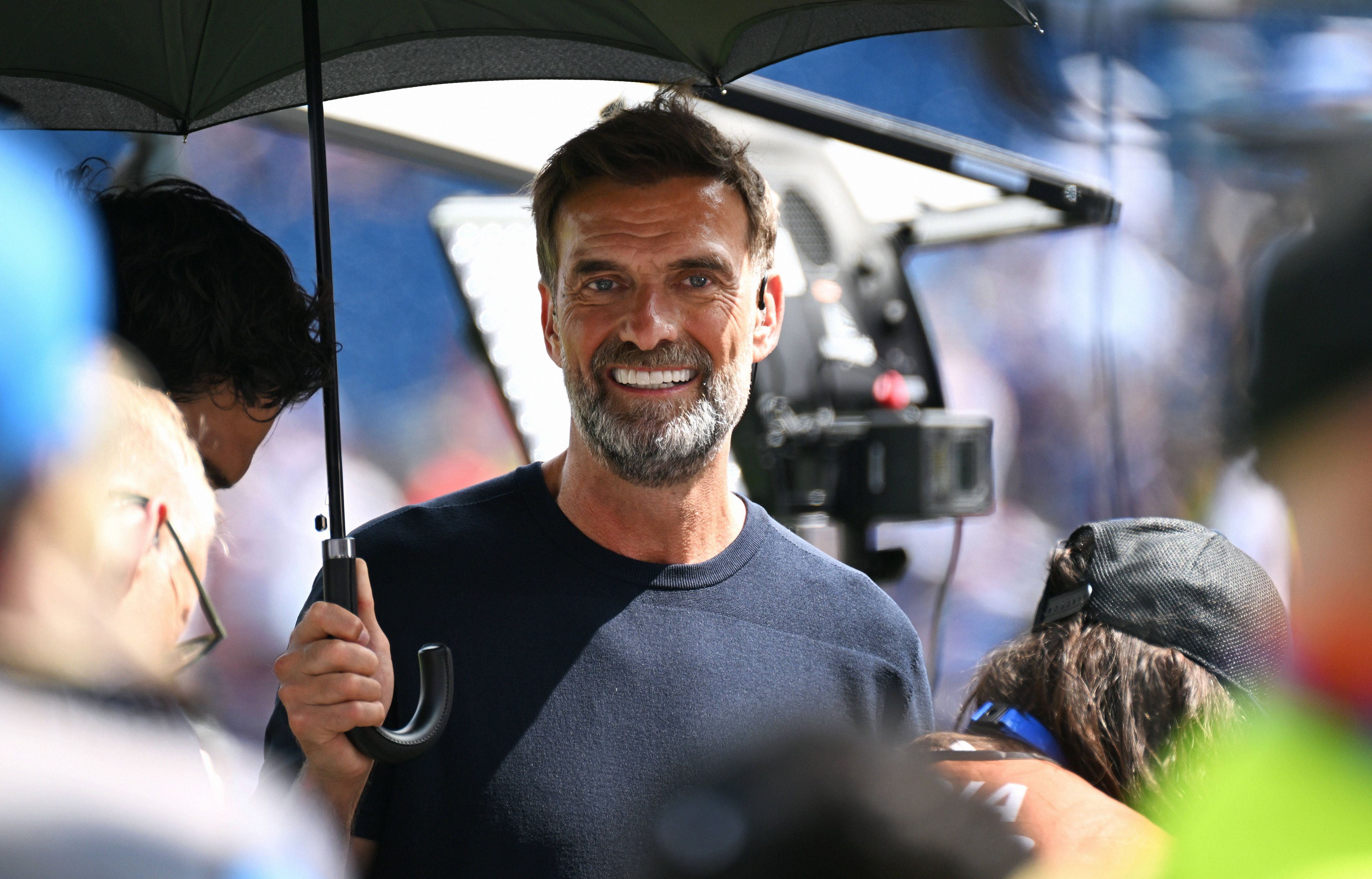 Jürgen Klopp steht als Experte bei einem Spiel zum Schutz vor der Sonne unter einem Schirm.