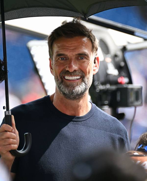 Jürgen Klopp steht als Experte bei einem Spiel zum Schutz vor der Sonne unter einem Schirm.
