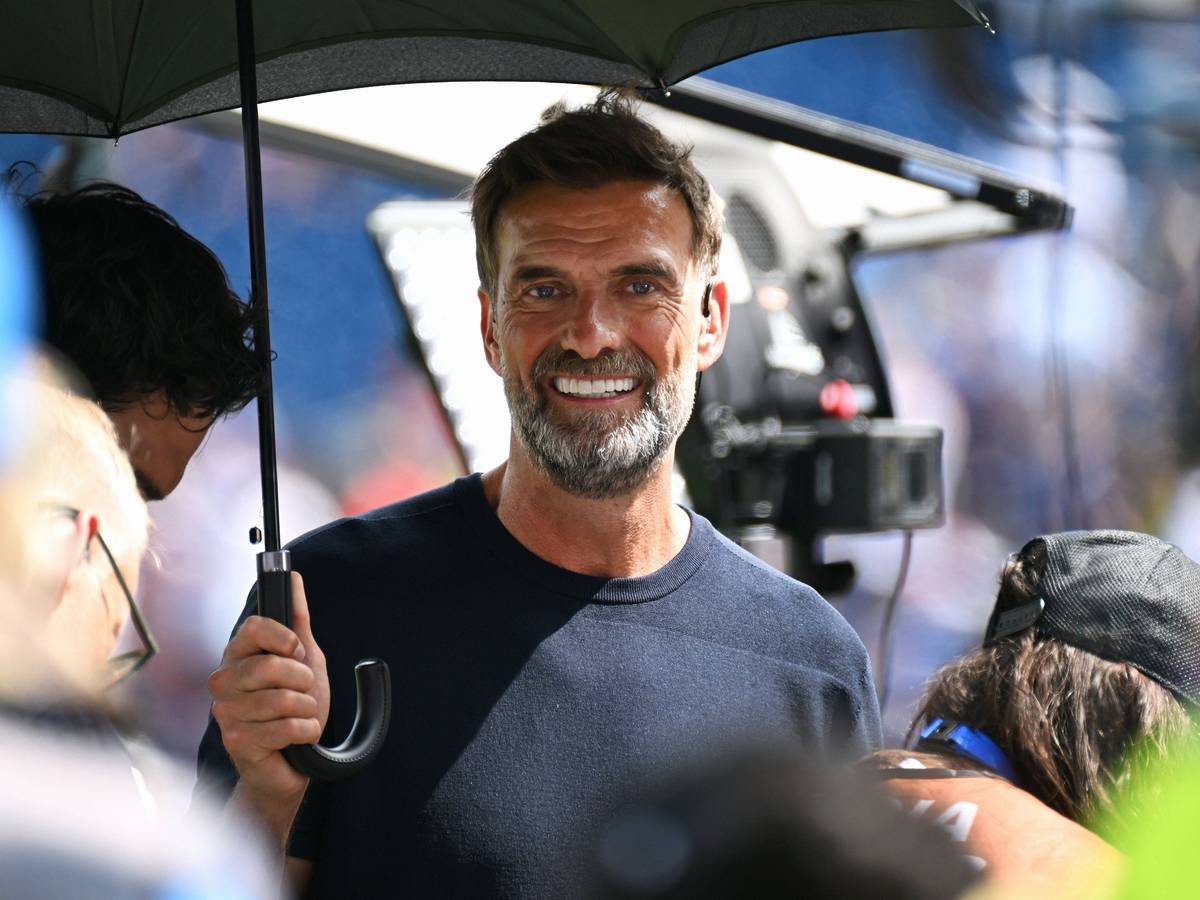 Jürgen Klopp steht als Experte bei einem Spiel zum Schutz vor der Sonne unter einem Schirm.